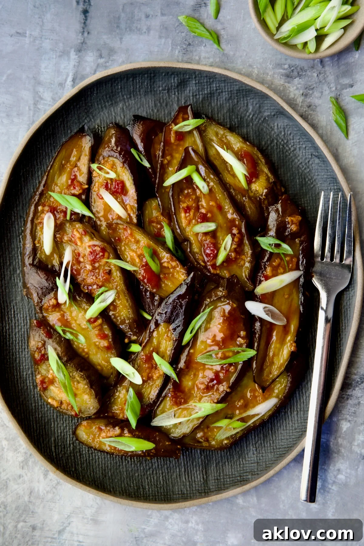 Thai Sweet Chili Glazed Eggplant Recipe 8 Thai Sweet Chili Eggplant on blue oval plate with fork garnished with scallions.
