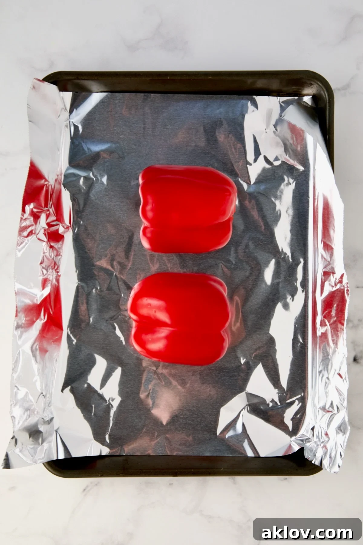 Two red bell pepper halves on aluminum foil-lined rimmed sheet pan before being roasted.
