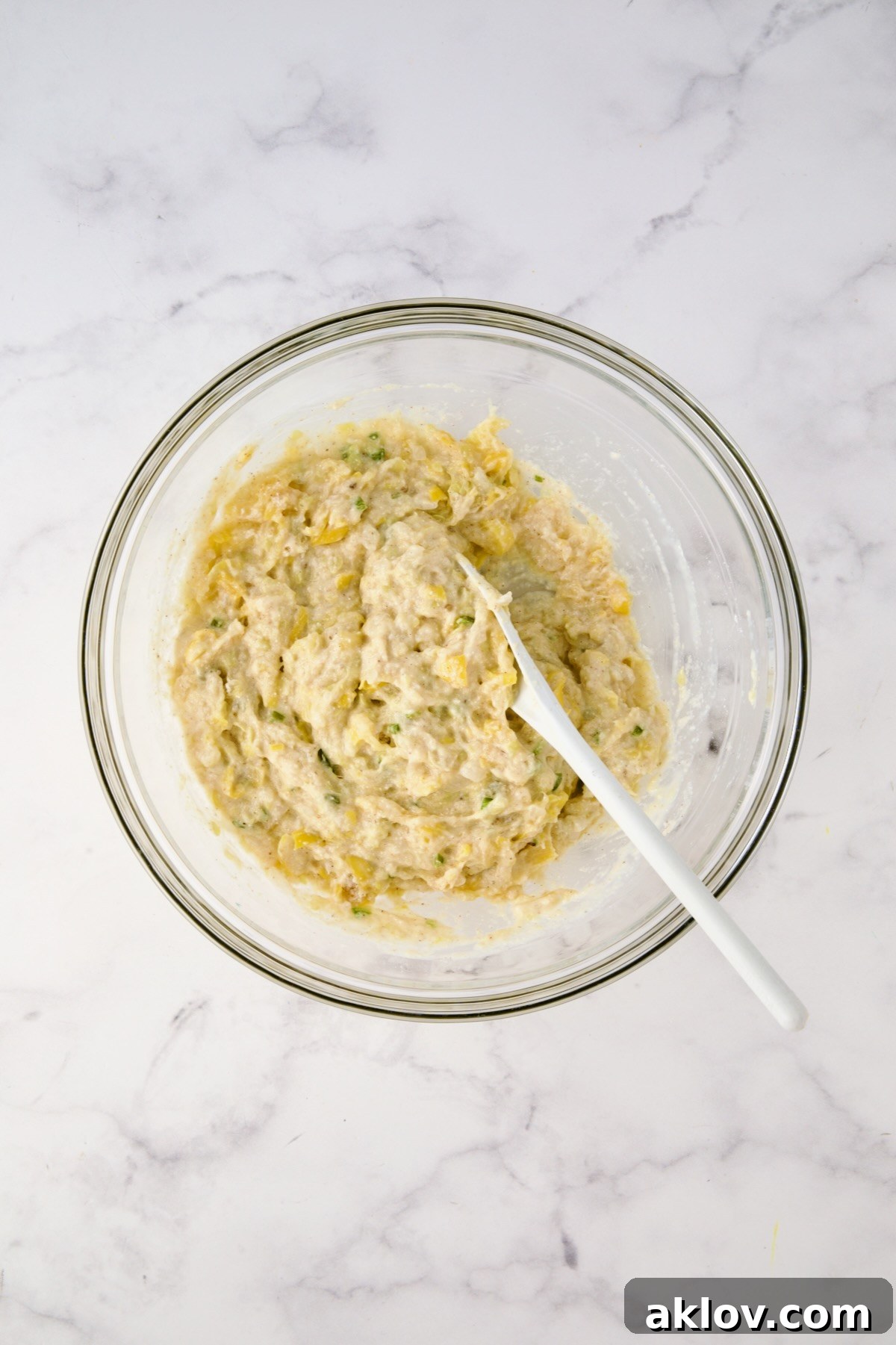 Batter for squash puppies mixed together in glass bowl with white mixing spoon.