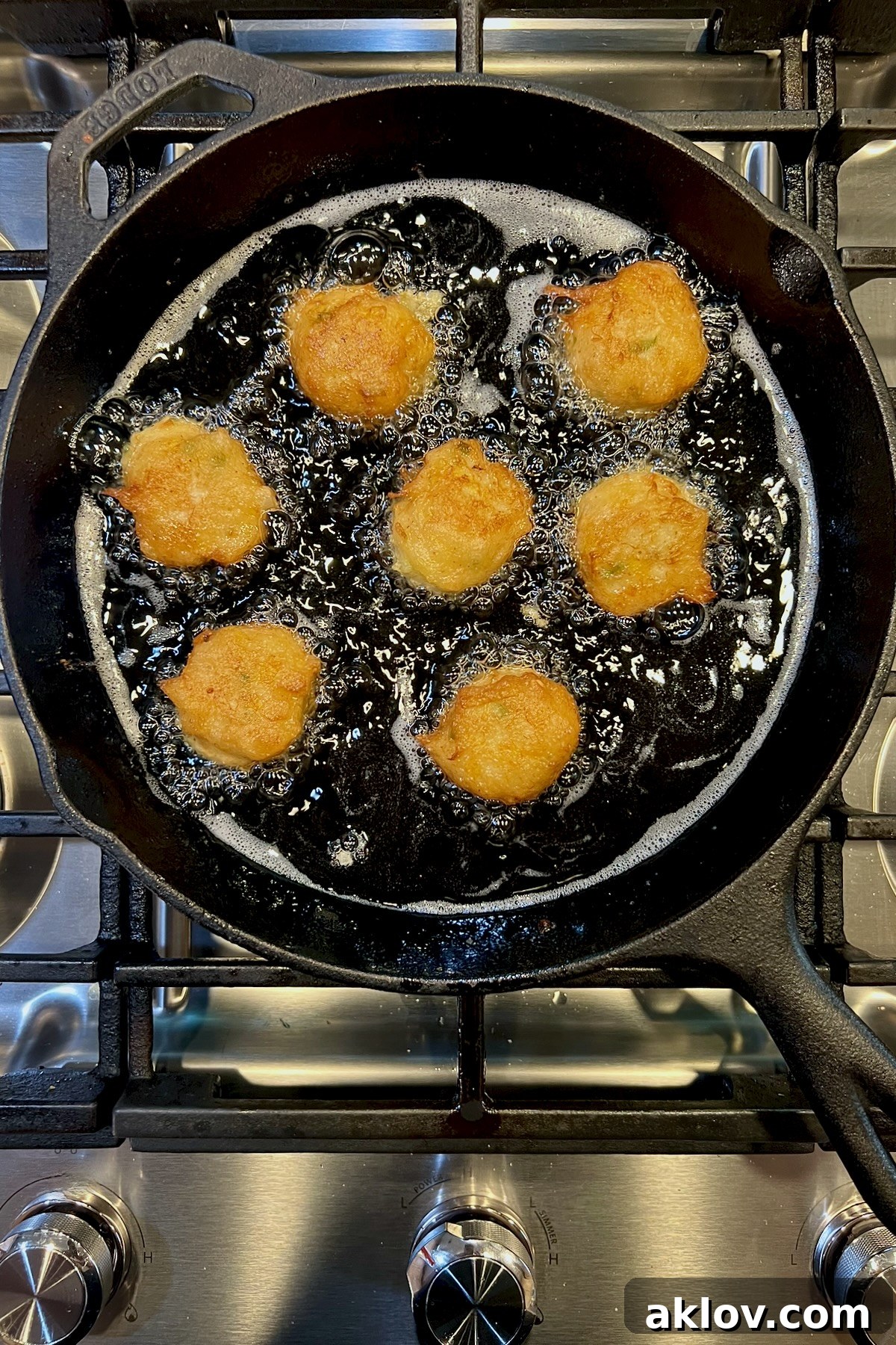 Seven squash puppies frying in a black cast iron skillet.