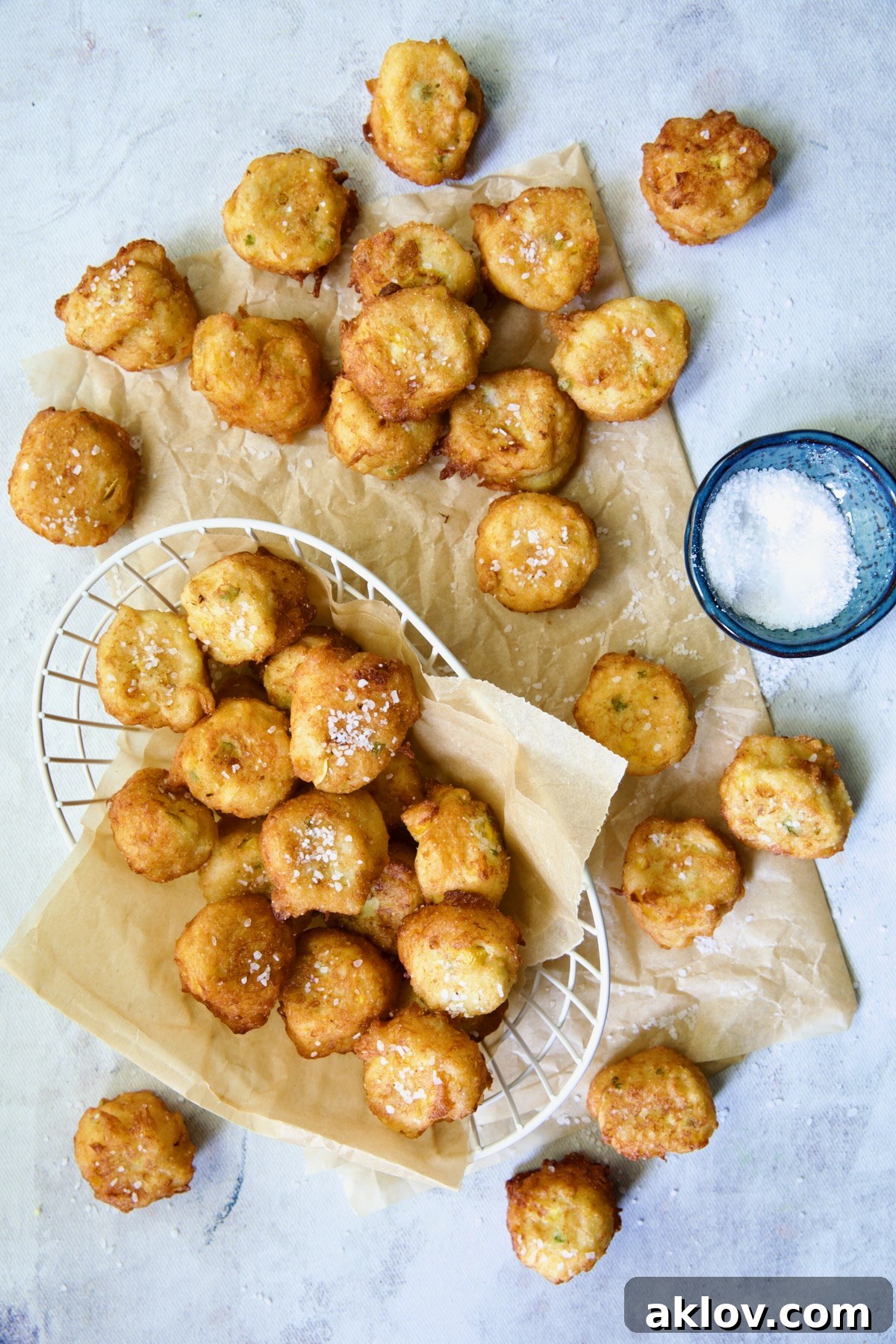 Fried squash puppies on parchment paper with some in a white wire basket.