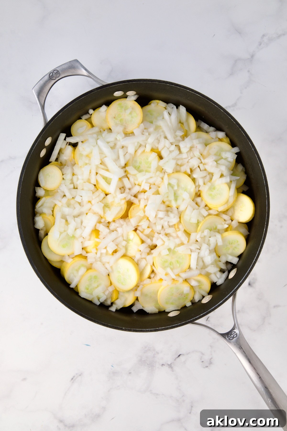 Uncooked sliced yellow squash and chopped onion in black skillet.