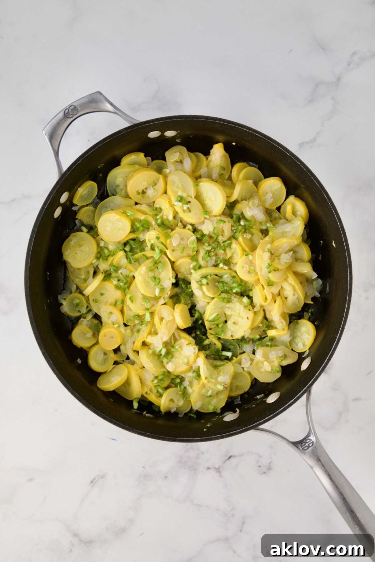 Uncooked sliced yellow squash, chopped onion and diced jalepeno in black skillet.