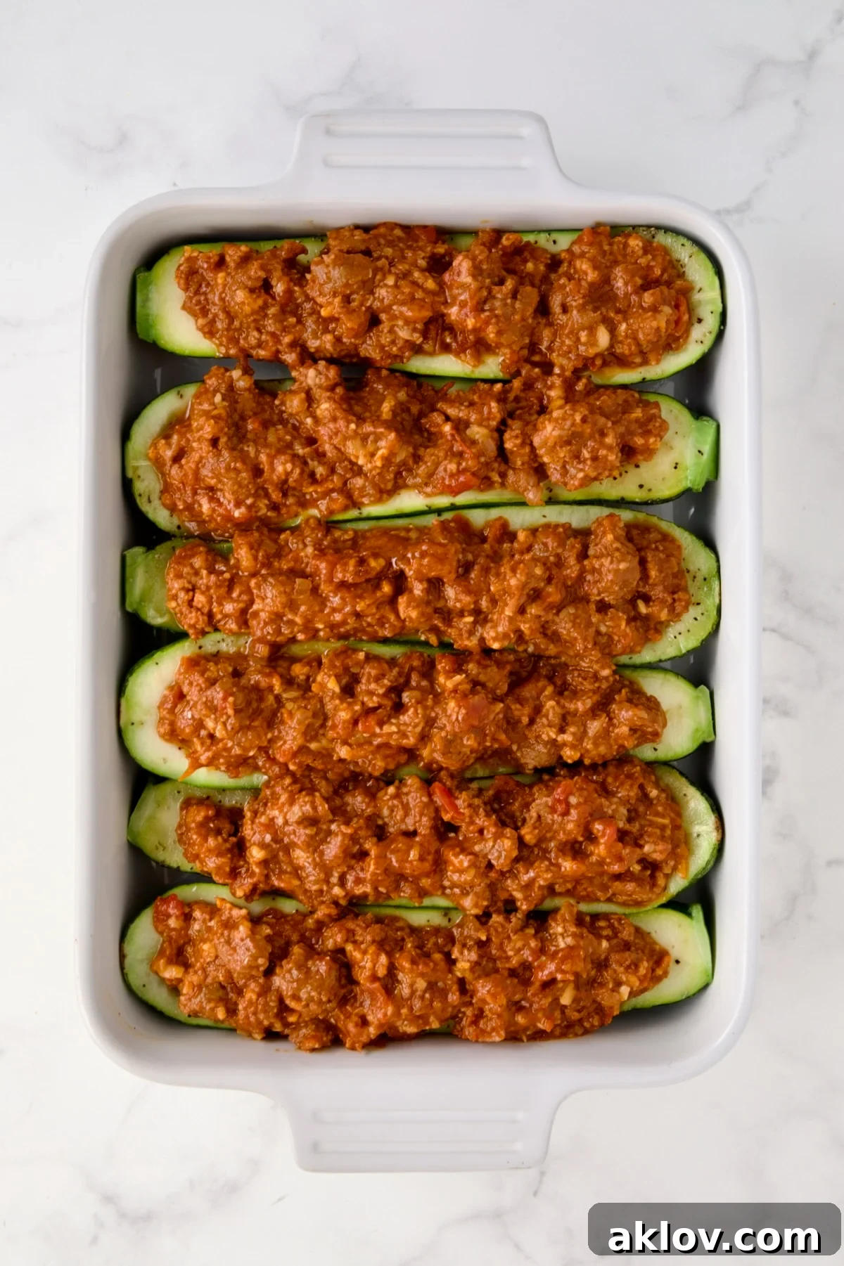 Six Chorizo-Stuffed Zucchini in white rectangular baking dish before being baked and before cheese is added.
