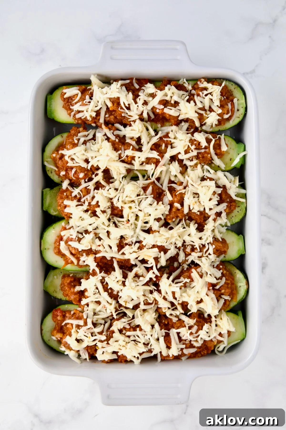 Six Chorizo-Stuffed Zucchini in white rectangular baking dish before being baked with cheese is added.