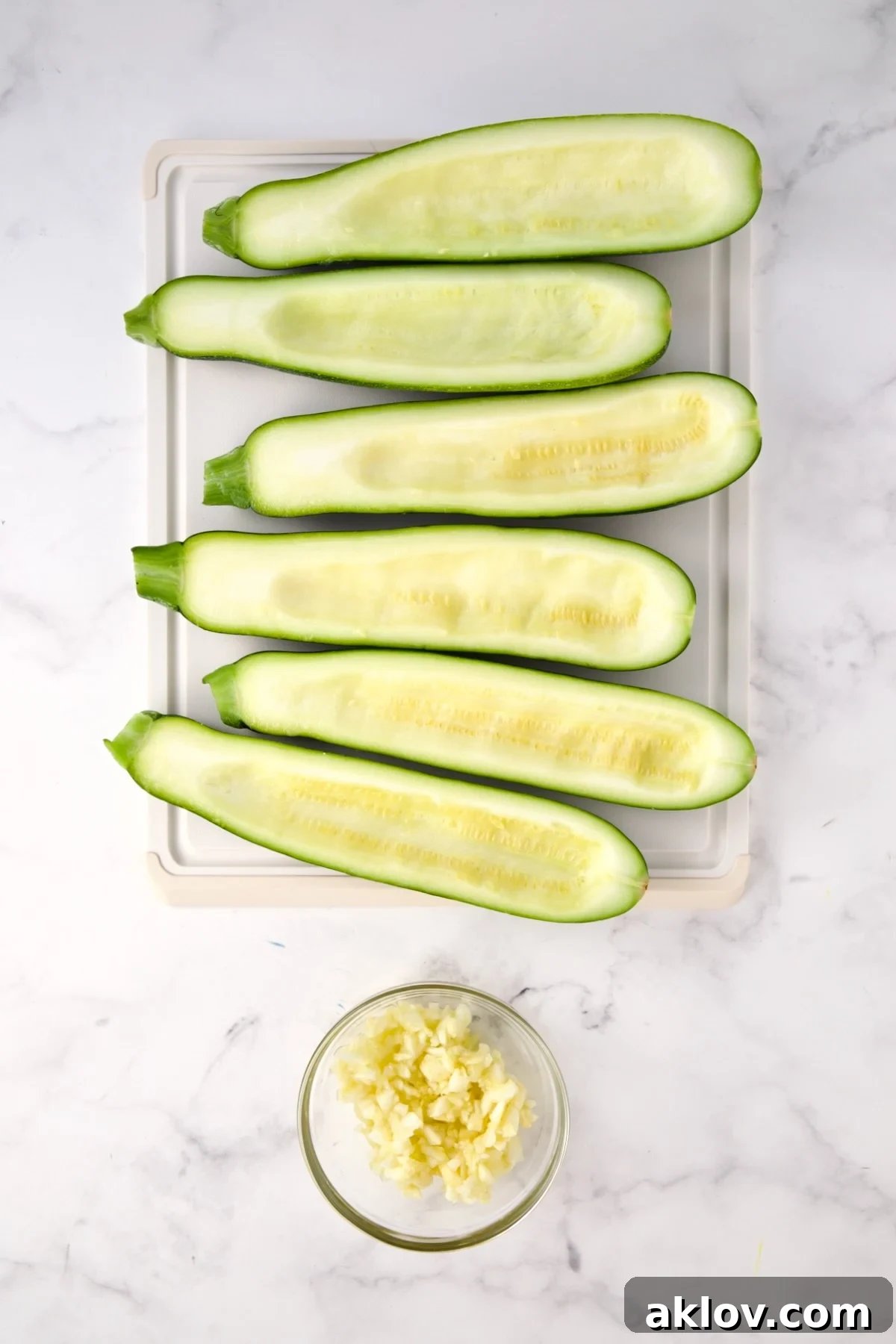 Six hollowed out zucchini halves on white plastic cutting board with the pulp in a small glass bowl.
