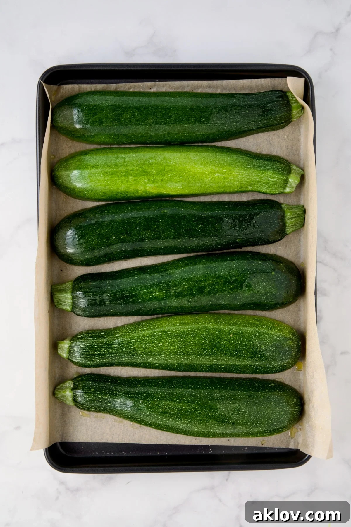 Six zucchini halves on parchment paper-lined rimmed baking sheet.