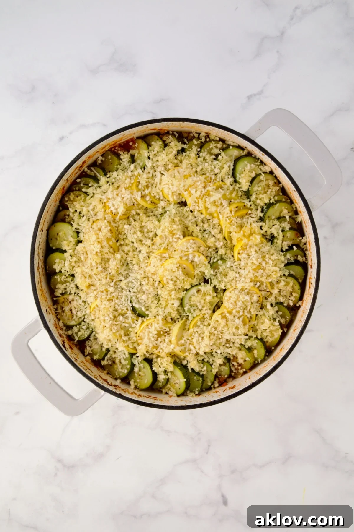 Breadcrumb mixture placed over zucchini and yellow squash in white enamel cast iron skillet.