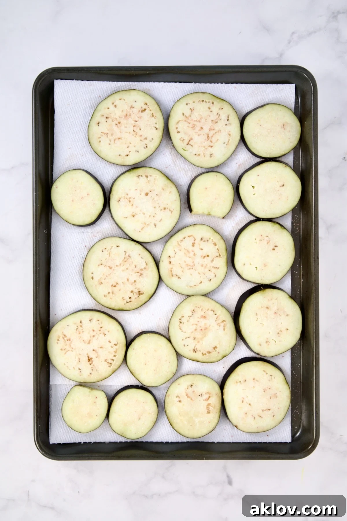 Eggplant slices on paper towel-lined rimmed baking sheet.