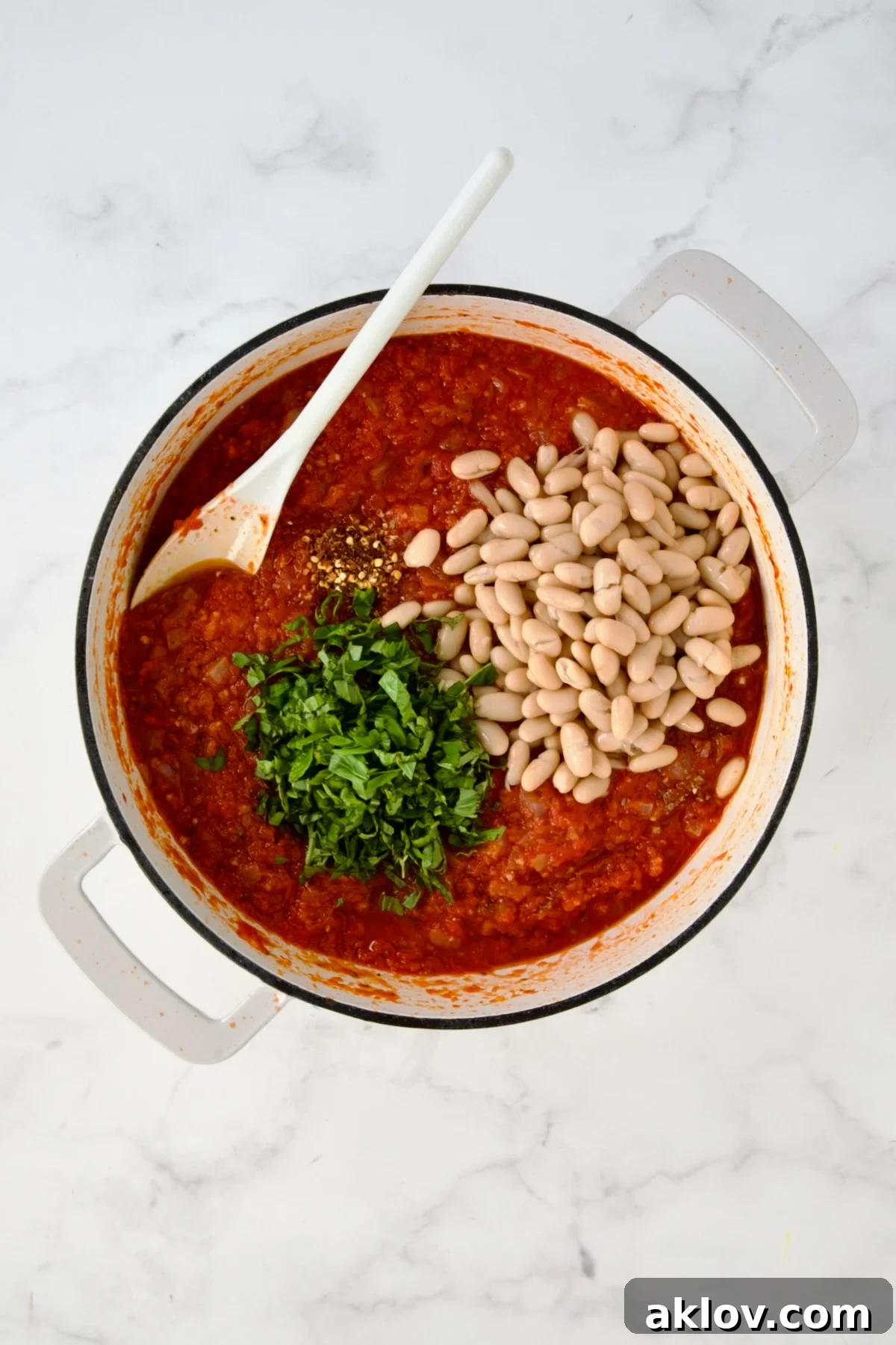 Fresh basil, beans and red pepper flakes added to tomato sauce in white enamel cast iron skillet.