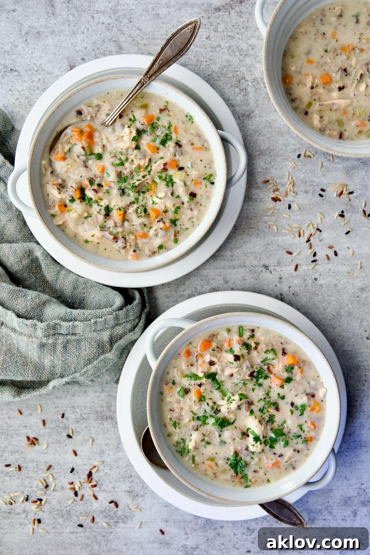 Three servings of Creamy Chicken and Wild Rice Soup in white bowl with spoon.