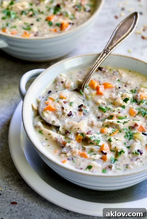 One serving of Creamy Chicken and Wild Rice Soup in white bowl with spoon.