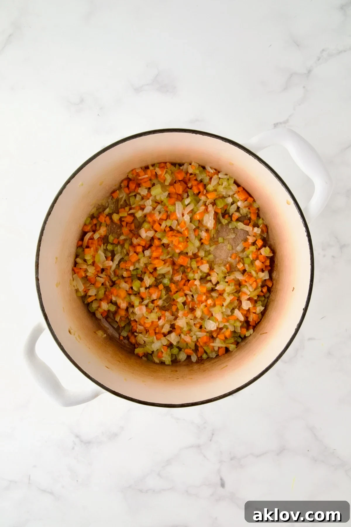 Cooked onion, carrot and celery in white enamel Dutch oven.